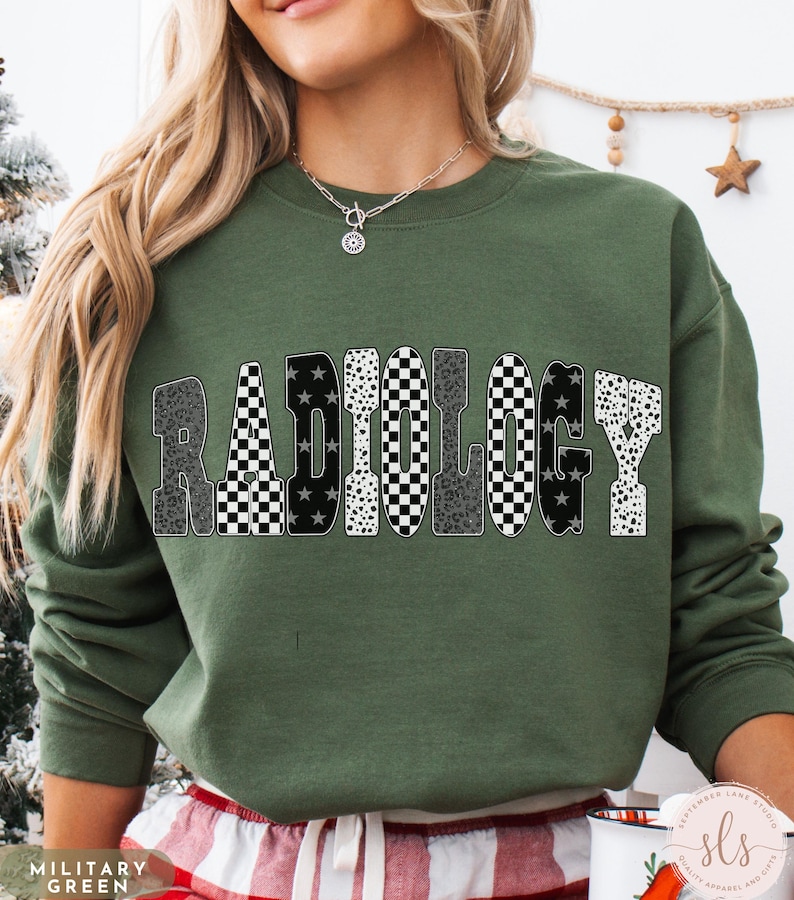 K&ouml;nnte beinhalten: Milit&auml;rgr&uuml;nes Sweatshirt mit dem Wort "RADIOLOGY" in einem auff&auml;lligen, gemusterten Design. Die Buchstaben zeigen eine Mischung aus Leopardenmuster, Schachbrettmuster und Sternenmustern. Das Sweatshirt ist ein Rundhals-Stil.