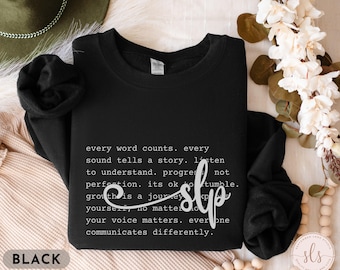 May include: Black sweatshirt with a white graphic print that reads "every word counts. every sound tells a story. listen to understand. progress not perfection. its ok to tumble. growth is a journey. your voice matters. everyone communicates differently."