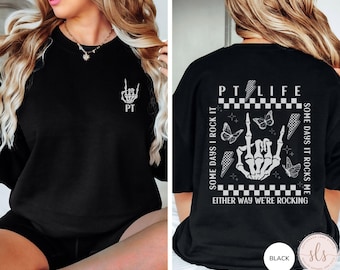 May include: Black sweatshirt with a white graphic print of a skeleton hand giving the rock and roll sign. The text "PTLIFE" is printed above the hand, and the text "SOME DAYS I ROCK IT SOME DAYS IT ROCKS ME EITHER WAY WE'RE ROCKING" is printed below the hand. The text "PT" is printed on the left side of the sweatshirt.