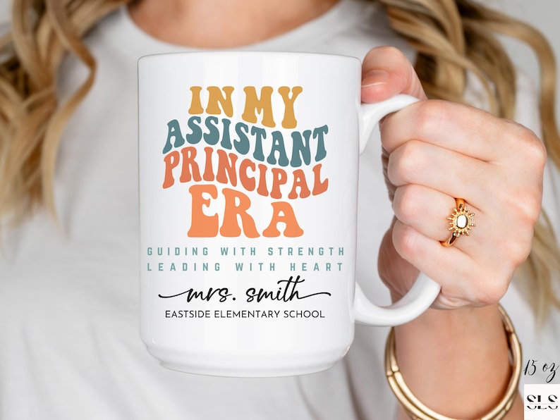 May include: White ceramic coffee mug with the text "IN MY ASSISTANT PRINCIPAL ERA GUIDING WITH STRENGTH LEADING WITH HEART mrs. smith EASTSIDE ELEMENTARY SCHOOL" in colorful retro font.