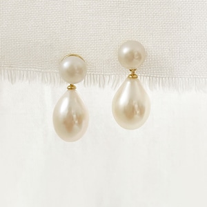 May include: A pair of pearl earrings. Each earring has a small, round pearl at the top, connected by gold-coloured metal to a larger, teardrop-shaped pearl. The pearls are creamy white and have a subtle lustre.