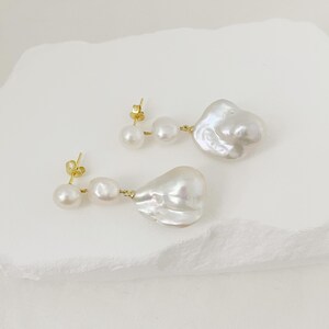 May include: A pair of earrings with three white pearls each. The earrings have a gold-coloured post and connecting wire. The largest pearl has an irregular, baroque shape.
