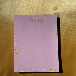 May include: Pink notepad with a floral border and the word "Notes" printed in orange at the top.