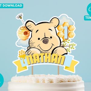 Puede incluir: Adorno para tarta con un oso de dibujos animados, el nombre "Nathan" y el número "1". El diseño incluye una colmena, panales y una abeja voladora, todo sobre un fondo azul claro.