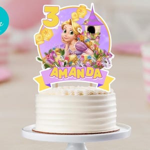 May include: A white cake topped with a Rapunzel-themed cake topper. The topper features a cartoon illustration of Rapunzel, the number 3, and the name "AMANDA" on a banner. The cake is on a white cake stand.