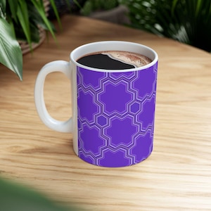 May include: A white coffee mug with a purple geometric pattern. The mug is filled with coffee.