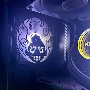 Pode incluir: Um ventilador de caixa de computador com um gráfico personalizado em preto e branco de um rosto de desenho animado com chamas. O ventilador é iluminado com uma luz branca.