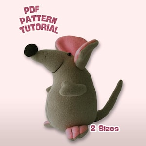 Puede incluir: Un ratón de peluche gris con orejas y pies rosas, una nariz negra y una larga cola. La imagen incluye el texto "PDF PATTERN TUTORIAL" y "2 Sizes". El ratón es un artículo hecho a mano.