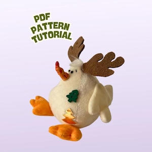May include: A whimsical, plush snowman-like figure with orange feet, a carrot nose, and brown antlers. A green tree and gold leaf are sewn on the body. The text "PDF PATTERN TUTORIAL" is in the upper left corner. This item is likely a handmade craft.