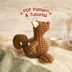 Puede incluir: Un peluche de ardilla de tela a cuadros marrón con una pequeña nariz a rayas rojas y blancas y orejas interiores blancas. Sobre la ardilla, el texto dice PDF Pattern & Tutorial en letras marrones con pequeños corazones naranjas.