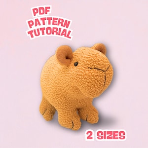 Puede incluir: Un peluche de color marrón claro con una superficie texturizada, orejas pequeñas y una cara cosida. La imagen incluye el texto "PDF PATTERN TUTORIAL" y "2 SIZES" en un diseño rosa y blanco.