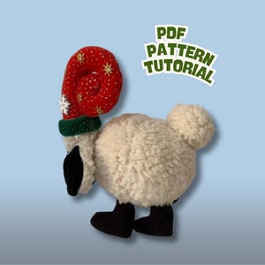 May include: A plush sheep toy with a red and white Christmas hat and black boots. The hat has gold stars and a white snowflake. The text "PDF PATTERN TUTORIAL" is in a green and white banner.