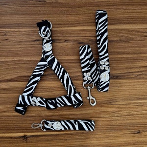 May include: A black and white zebra print dog harness and leash set with silver accents. The harness has a buckle closure and the leash has a clip.