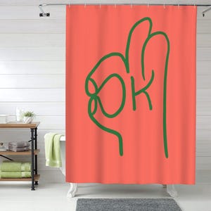 Puede incluir: Una cortina de ducha rosa coral con un contorno verde de un gesto de mano OK. El gesto de la mano está estilizado y la palabra "OK" está escrita dentro del círculo.