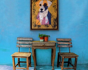 May include: A framed dog portrait with a brown wooden frame hangs on a blue wall. The artwork features a collage-style image of a dog with orange, white, blue, and pink elements. Below, a small wooden table and two chairs are visible.