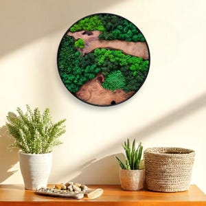 Könnte beinhalten: Runde Wandkunst mit schwarzem Rahmen, gefüllt mit einer Mischung aus grünem Moos und Holzelementen. Das Kunstwerk ist an einer cremefarbenen Wand angebracht. Das Stück bringt ein natürliches Element in den Raum. Ein dekoratives Stück für jedes Interieur.