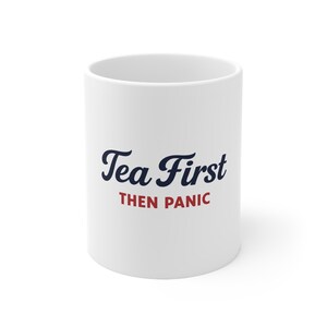 Puede incluir: Taza de cerámica blanca con el texto "Tea First THEN PANIC" en letras azul marino y rojo. La taza tiene forma cilíndrica y un diseño sencillo, adecuada para bebidas calientes.