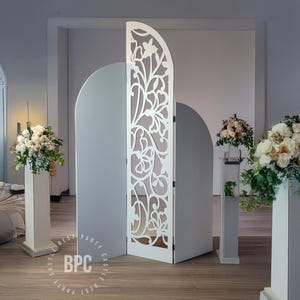May include: White archway backdrop with a decorative cutout design. The archway is made of two panels that can be used separately or together. The backdrop is ideal for weddings, parties, and other special events.