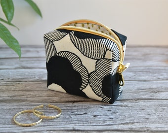May include: A small, square-shaped zippered pouch with a black and white geometric pattern. The pouch is open and the zipper is gold.