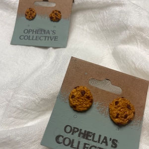 Puede incluir: Un par de pendientes en forma de galleta marrón y blanca en una tarjeta con el texto "Ophelia's Collective".
