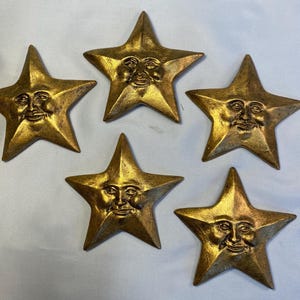 Conjunto de 5 estrellas doradas decorativas para pared; cada una está hecha a mano, acabada y pintada. Tiene un orificio en la parte posterior para colgarla.