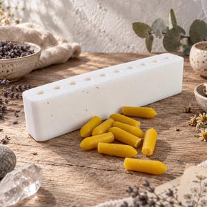 White reusable silicone suppository mold with multiple cavities shown beside finished yellow wax samples, styled with dried herbs and crystals for DIY home crafting and suppository making