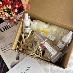 Top view of soy candle making kit components in a box, including essential oils, wax, flowers, and colorants in clear labeled pouches, ideal for DIY natural candles.