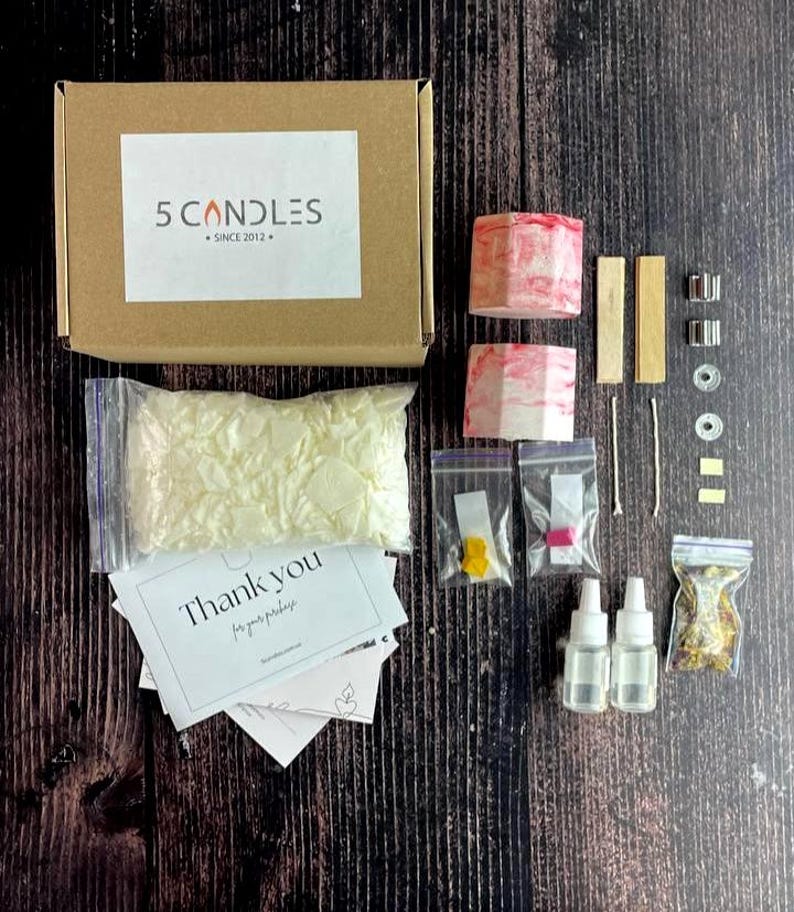 Full candle kit with red marble containers, soy wax, dyes, oils, and flowers laid out neatly