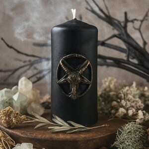Handmade black beeswax candle featuring a golden Baphomet emblem, placed on a wooden altar with crystals, herbs, and twigs, symbolizing protection, wisdom, and spiritual balance.