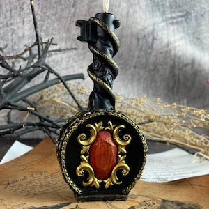 Black wax candle shaped like a gothic key with golden serpent and ornate red centerpiece on vintage parchment