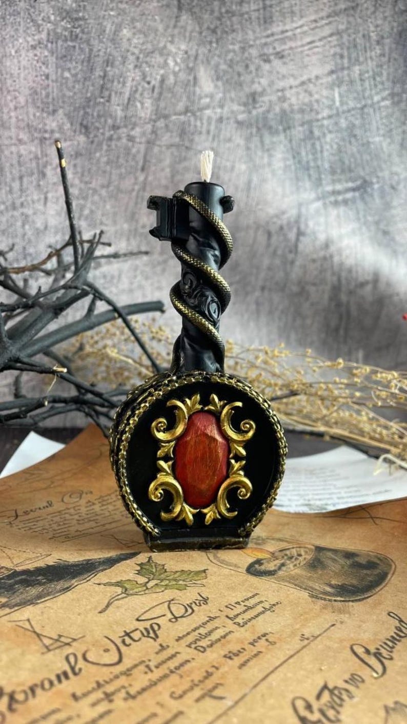 Black wax candle shaped like a gothic key with golden serpent and ornate red centerpiece on vintage parchment