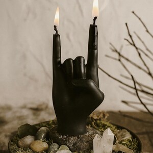 Black hand-shaped candle with two flames forming the rock gesture, placed on a moss and crystal altar setup, symbolizing creative energy and bold individuality in gothic rock-inspired decor.