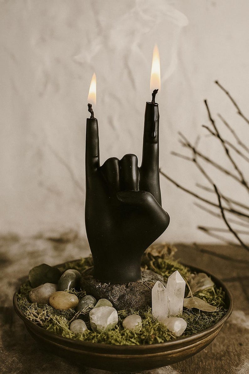Black hand-shaped candle with two flames forming the rock gesture, placed on a moss and crystal altar setup, symbolizing creative energy and bold individuality in gothic rock-inspired decor.