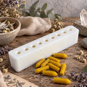 White reusable silicone suppository mold with multiple cavities beside finished yellow wax suppository samples, styled with dried herbs, lavender and quartz crystals for DIY crafting and home remedy preparation
