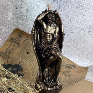 Bronze Lucifer-shaped candle burning next to tarot cards and crystals on a dark wooden surface, creating a mystical and dramatic atmosphere.