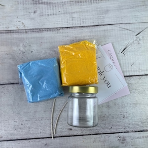 May include: A candle making kit with a glass jar, blue and yellow wax flakes, and two wicks. The kit also includes a thank you card.