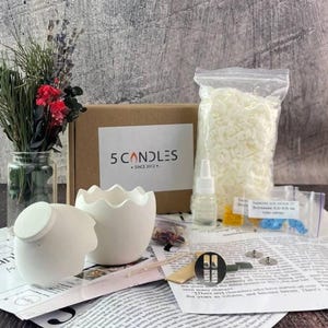 May include: A candle-making kit with a white egg-shaped candle holder and a matching lid. The kit includes a bag of wax, fragrance oil, wicks, and other supplies. The box has the text "5 Candles Since 2012".