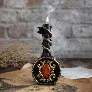 Black ritual candle shaped like an ornate key with gold details and red gemstone, lit and surrounded by vintage papers and mystical decor, creating a magical atmosphere.