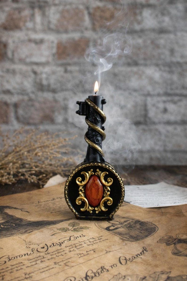 Black ritual candle shaped like an ornate key with gold details and red gemstone, lit and surrounded by vintage papers and mystical decor, creating a magical atmosphere.