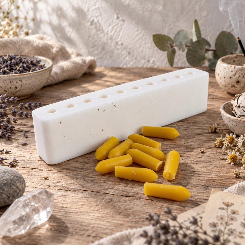White reusable silicone suppository mold with multiple cavities shown beside finished yellow wax samples, styled with dried herbs and crystals for DIY home crafting and suppository making