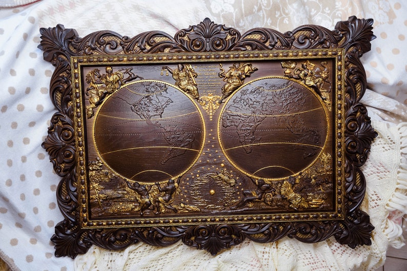 Puede incluir: Un marco de madera marr&oacute;n oscuro con tallas ornamentadas rodea dos globos dorados que representan un mapa del mundo. Los globos est&aacute;n colocados sobre un fondo marr&oacute;n oscuro con acentos dorados.
