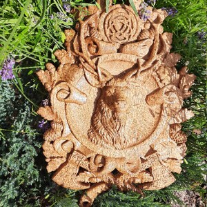 May include: A wooden wall plaque with a carved stag head surrounded by a wreath of leaves, acorns, and other woodland motifs. The plaque is painted in a warm brown color.