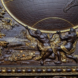 Puede incluir: Una placa de madera marr&oacute;n oscuro con marco dorado y una escultura en relieve de dos figuras sosteniendo un globo terr&aacute;queo. El globo est&aacute; rodeado de estrellas y nubes.