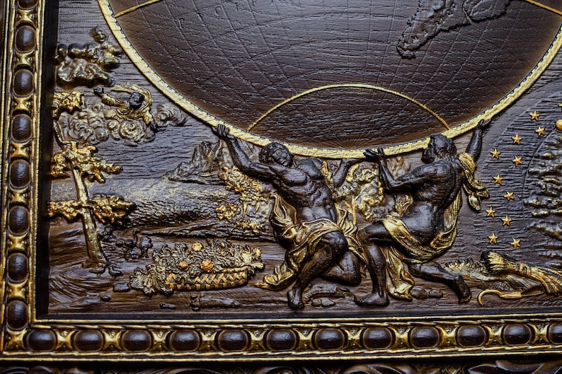 Puede incluir: Una placa de madera marr&oacute;n oscuro con marco dorado y una escultura en relieve de dos figuras sosteniendo un globo terr&aacute;queo. El globo est&aacute; rodeado de estrellas y nubes.
