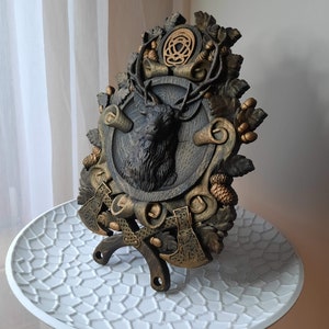 May include: A wooden wall plaque with a carved deer head, two axes, and a Celtic knot design. The plaque is painted in shades of brown and gold.