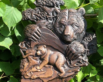 May include: A detailed, wooden carving depicting a bear and its cub in a forest setting. The artwork features a bear's head, a cub, and a tree, all carved with intricate detail. The wood has a rich, brown color.