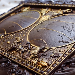 Puede incluir: Un marco de madera marr&oacute;n oscuro con detalles dorados, que presenta dos mapas del mundo en relieve, en relieve. El marco tiene tallas intrincadas y un dise&ntilde;o detallado.