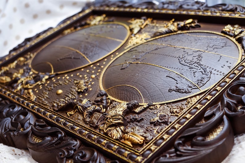 Puede incluir: Un marco de madera marr&oacute;n oscuro con detalles dorados, que presenta dos mapas del mundo en relieve, en relieve. El marco tiene tallas intrincadas y un dise&ntilde;o detallado.