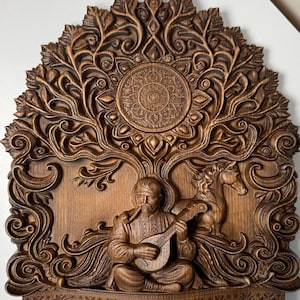 Op de afbeelding: Een gedetailleerde, bruine houten snijwerk met een zittende figuur die een snaarinstrument bespeelt, met een paard en een boomachtig ontwerp. Het snijwerk heeft ingewikkelde details en een cirkelvormig patroon aan de bovenkant, met een volkskunstthema.