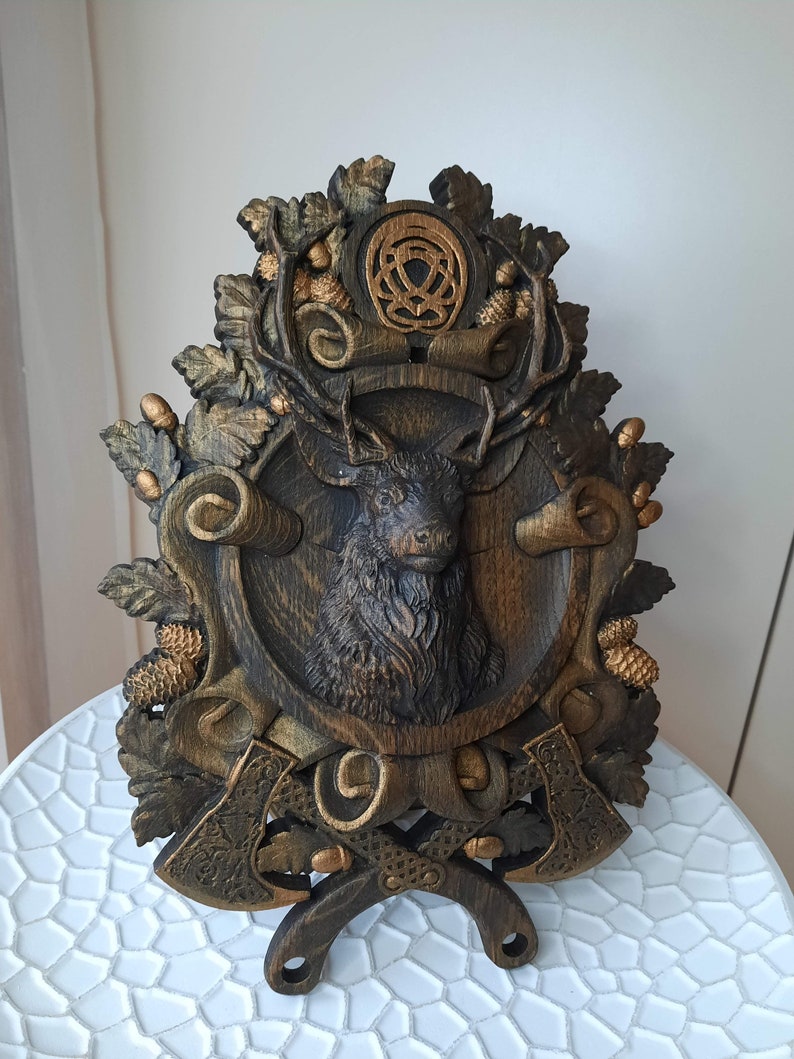 May include: A wooden wall plaque with a carved deer head, surrounded by leaves and acorns. Two crossed axes are at the bottom of the plaque, with a Celtic knot design at the top.